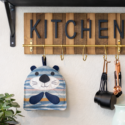 Wooden kitchen sign with 'KITCHEN' and hooks on a wall above a counter.