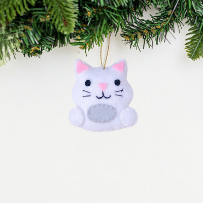 Cat-shaped ornament with pink ears and nose on a white background with Christmas tree branches.