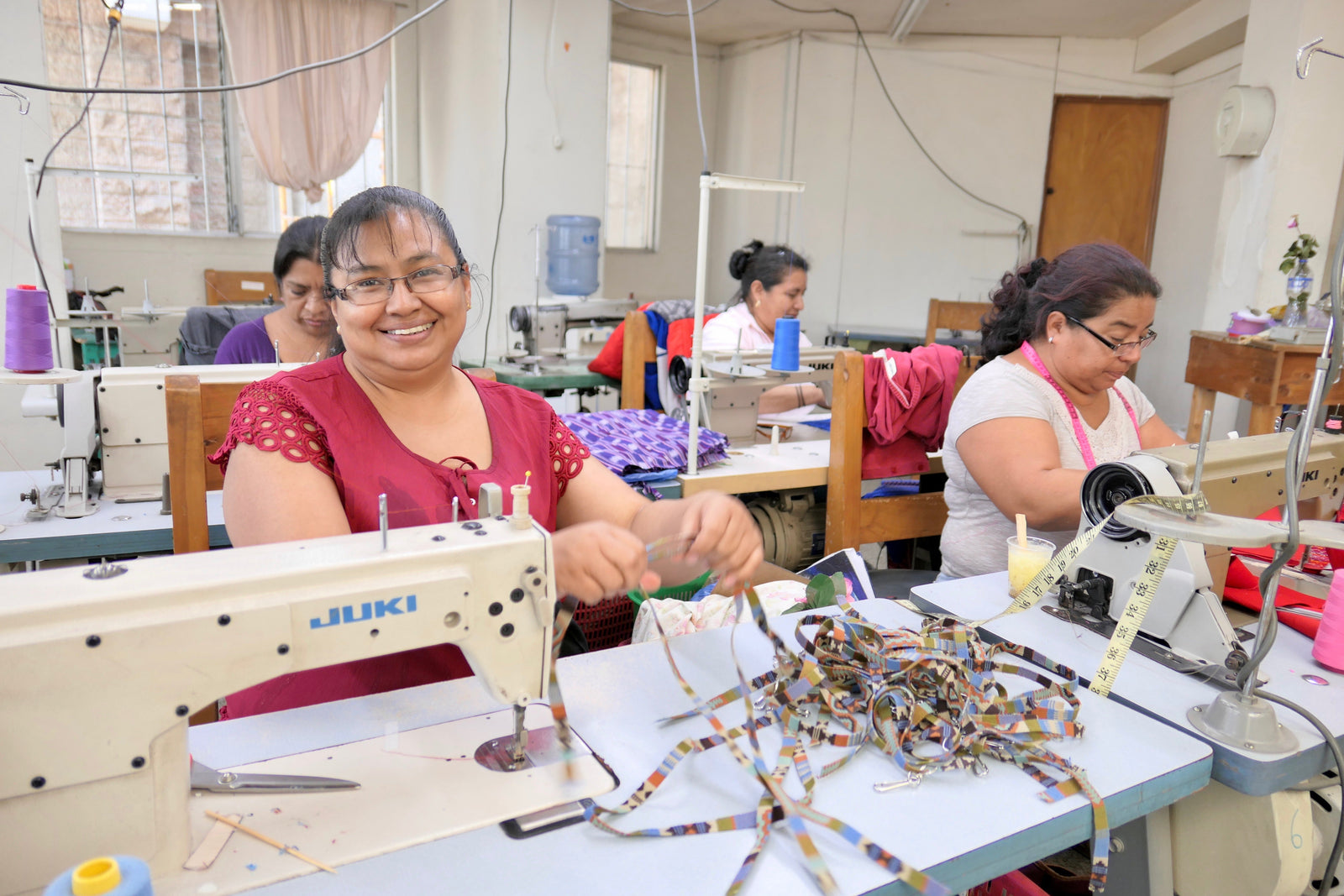 UPAVIMA producers sit at sewing machines sew fair trade products in Guatemala City. The woman on the left looks into the camera smiling.
