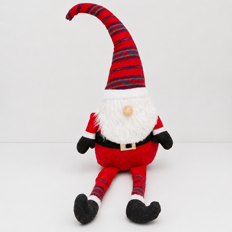 Decorative gnome with striped hat on a shelf with Christmas decorations and a snowy view outside.