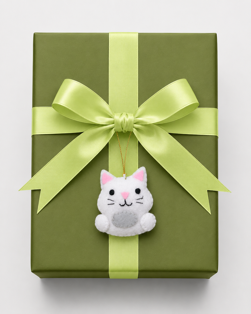 Cat-shaped ornament with pink ears and nose on a white background with Christmas tree branches.