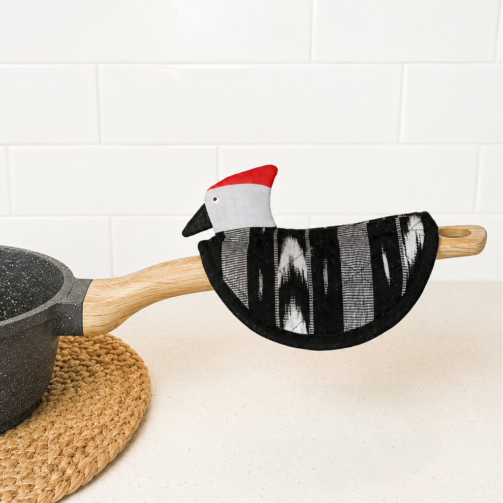 Potholder with a cartoon chicken design on a pot handle against a white tiled wall.